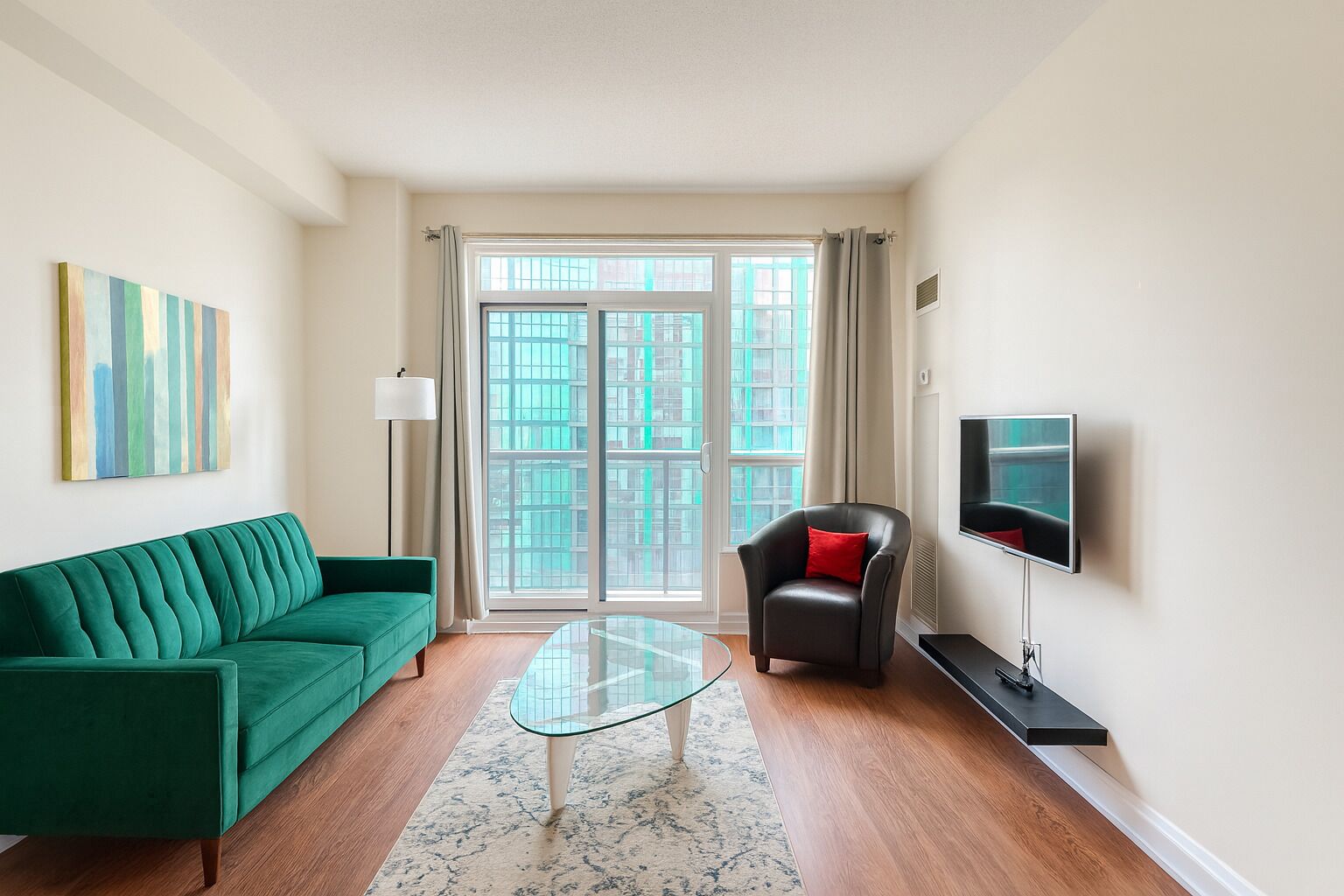 A modern living room with a green sofa, a glass coffee table, a leather armchair, and a TV on a stand.