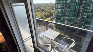 Un balcone con tavolo e sedie, vista su un paesaggio urbano con edifici e aree verdi.