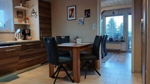 A modern kitchen with wooden cabinets, a dining table with chairs, and a view of the outdoors through a large window. - NEW! Modern living in Erbendorf - Upper Palatinate (Erbendorf)