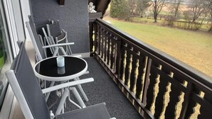 A balcony with a table and chairs, a decorative railing, and a view of a grassy area with trees. - NEW! Modern living in Erbendorf - Upper Palatinate (Erbendorf)
