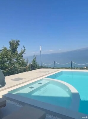 Un cielo azul despejado, una piscina con vistas a las montañas y un área cercada con árboles.