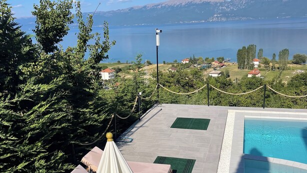 A pool area with a view of a lake and mountains. There are lounge chairs and a canopy. - Bella Vista Lake Villa • Jacuzzi • Balcony • Perfect for Groups (Memlisht)
