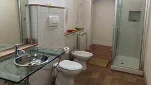 Une salle de bain avec un lavabo en verre, des toilettes, un bidet et une douche à parois de verre.