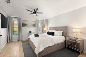 Ein Schlafzimmer mit einem Bett, einem Nachttisch, einer Lampe, einem Deckenventilator und einem Fenster mit Vorhängen.