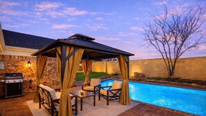 Eine Terrasse im Freien mit Pool, überdachter Sitzgruppe und Grill.