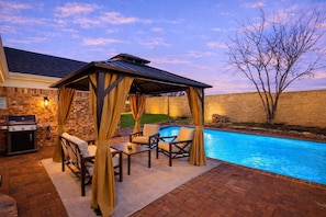 Eine Terrasse im Freien mit Pool, überdachter Sitzgruppe und Grill.