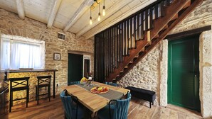 Un interior rústico con una mesa de comedor de madera, sillas azules, una escalera y paredes de piedra.