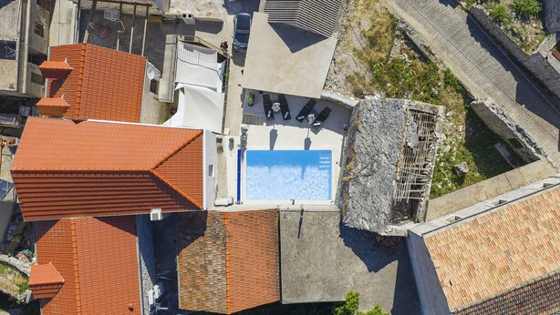 Vista aérea de una propiedad con piscina, terraza cubierta y muro de piedra.