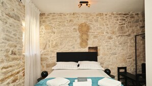 Un dormitorio con pared de piedra, cama con ropa blanca y colcha azul, y un cartel de bienvenida.