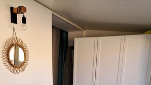 Ein Zimmer mit einem Holztisch, einem grauen Stuhl, einem weißen Wandschrank und einem wandmontierten Spiegel mit Leuchte.