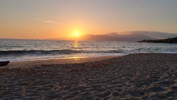 Ein Strand bei Sonnenuntergang, ruhiges Meer und ferne Berge.