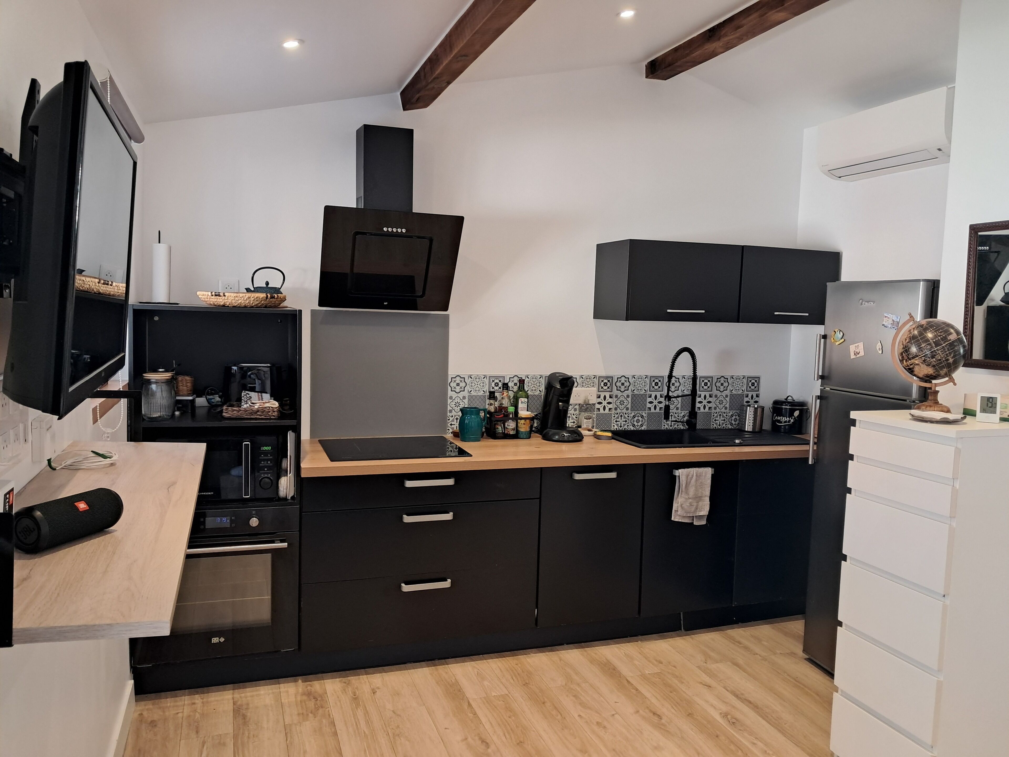 A modern kitchen with black cabinets, a wooden countertop, a built-in oven, and a microwave.