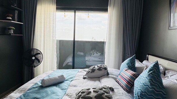 Et hotelværelse med seng, ventilator, et vindue med gardiner og udsigt ud.