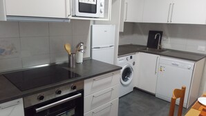 Cocina compacta con microondas, horno, lavadora y un pequeño comedor con una silla.