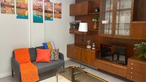 Una sala de estar moderna con un sofá gris, cojines coloridos, una mesa de centro de vidrio, un mueble de madera con puertas de cristal y un televisor de pantalla plana.