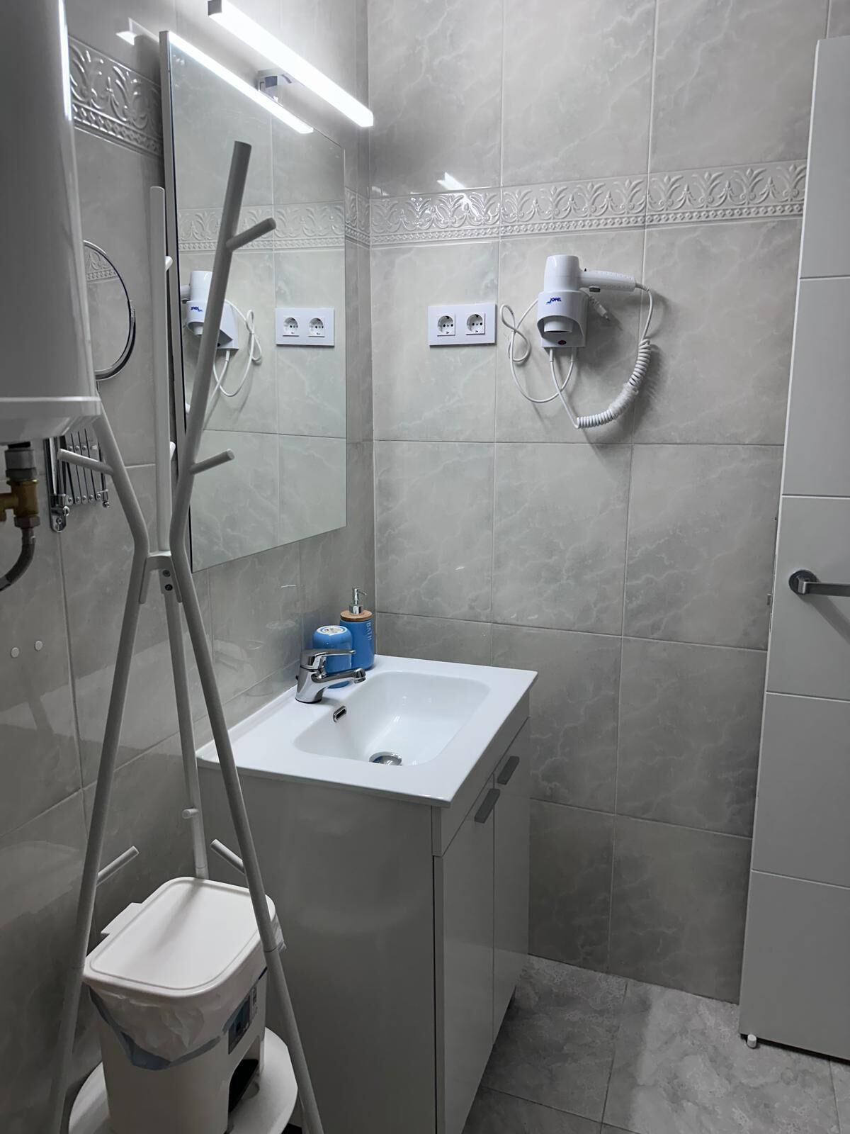 Un baño moderno con un lavamanos blanco, un espejo, un secador de pelo y un carrito de limpieza.