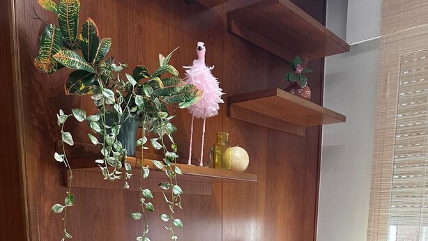 Un aparador de madera con un regador rosa, un florero con flores y un flamenco decorativo.
