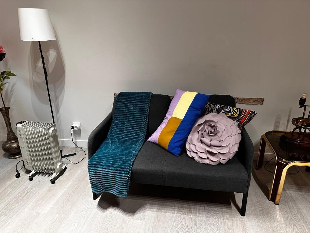 Una sala de estar moderna con un sofá negro, una manta color turquesa y almohadas coloridas.