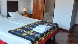 A hotel room with a bed, a wooden door, a nightstand, and a wall with two paintings.