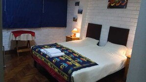 A bedroom with a bed, a nightstand, a table with a red cloth, and a wall with a painting.