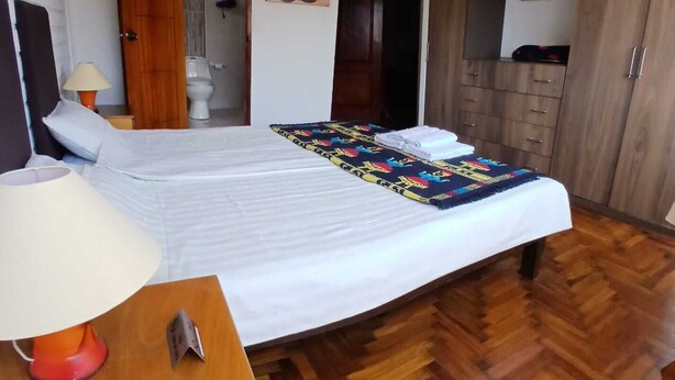 A hotel room with a large bed, wooden wardrobe, and a bathroom visible through an open door.