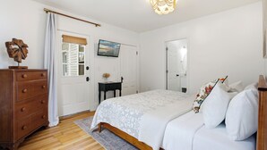 A bedroom with a bed, dresser, television, and a door with a window. - Boothbay Harbor King Suite  - Room 13 at AQ Inn - Fireplace, Patio, Harbor View! (Boothbay Harbor)