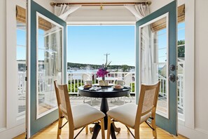 A balcony with a table set for two, a vase with flowers, and a view of a residential area. - Boothbay Harbor King Suite  - Room 13 at AQ Inn - Fireplace, Patio, Harbor View! (Boothbay Harbor)