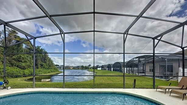 Zona de piscina con una sección cubierta y vistas a un elemento acuático y edificios al fondo.