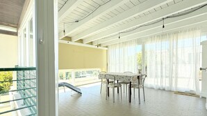 Ein Balkon mit Tisch und Stühlen, Blick ins Freie und eine Tür zu einem anderen Raum.