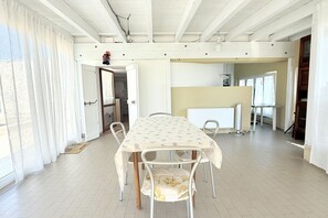 Een eetgedeelte met een tafel en stoelen, een keuken op de achtergrond en een deur die naar een andere kamer leidt.