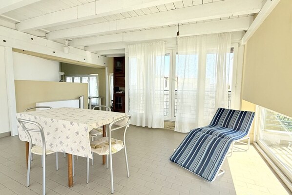 Een kamer met een eettafel, stoelen, een gestreept fauteuil en een balkon met uitzicht.