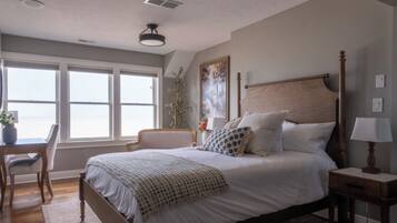 A bedroom with a large bed, a bedside table, a chair, and a window.