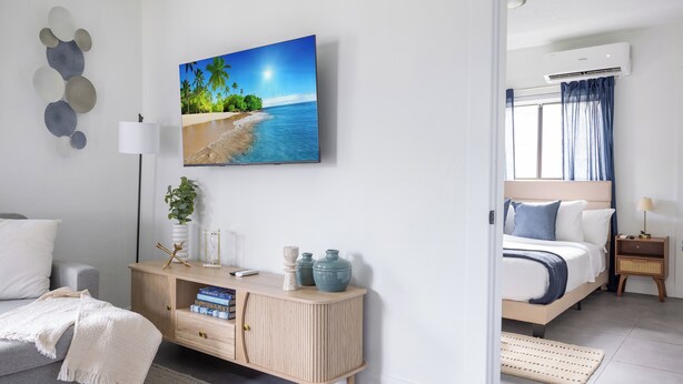 A modern bedroom with a bed, bedside table, lamp, and a wall-mounted TV displaying a beach scene. - Unit 4 - Beautiful 1BR Apt w/Parking Near Biscayne Boulevard (Miami)