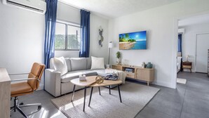 A modern living room with a sofa, a coffee table, a chair, and a painting of a beach scene. - Unit 4 - Beautiful 1BR Apt w/Parking Near Biscayne Boulevard (Miami)