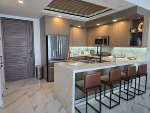 A modern kitchen with a central island, stainless steel appliances, and a bar area with stools. - Experience Paradise at Encantame Soleil Beach! (Puerto Peñasco)