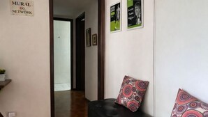 Ein Flur mit einem grünen Sofa und einem schwarzen Sofa, einem Holzboden mit Fischgrätmuster und einer Tür zu einem anderen Raum.