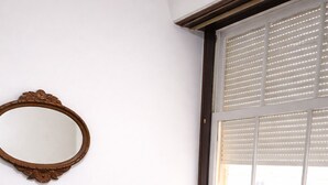 Ein Schlafzimmer mit einem Bett, einem spiegelnden Wandbild aus Holz und einem Fenster mit Jalousien.