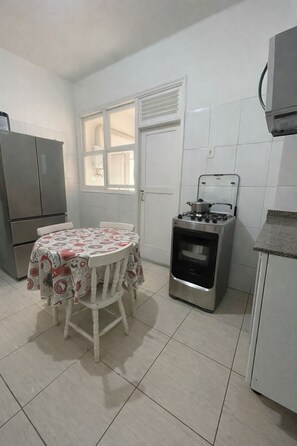 A small kitchen with a dining table, a refrigerator, a stove, and a window. - JULIANA'S ROOM AT HOME (Rio de Janeiro)
