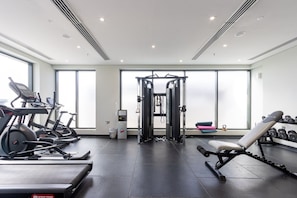 Et moderne fitnesscenter med løbebånd, styrketræningsudstyr og et stort vindue, der lukker naturligt lys ind.