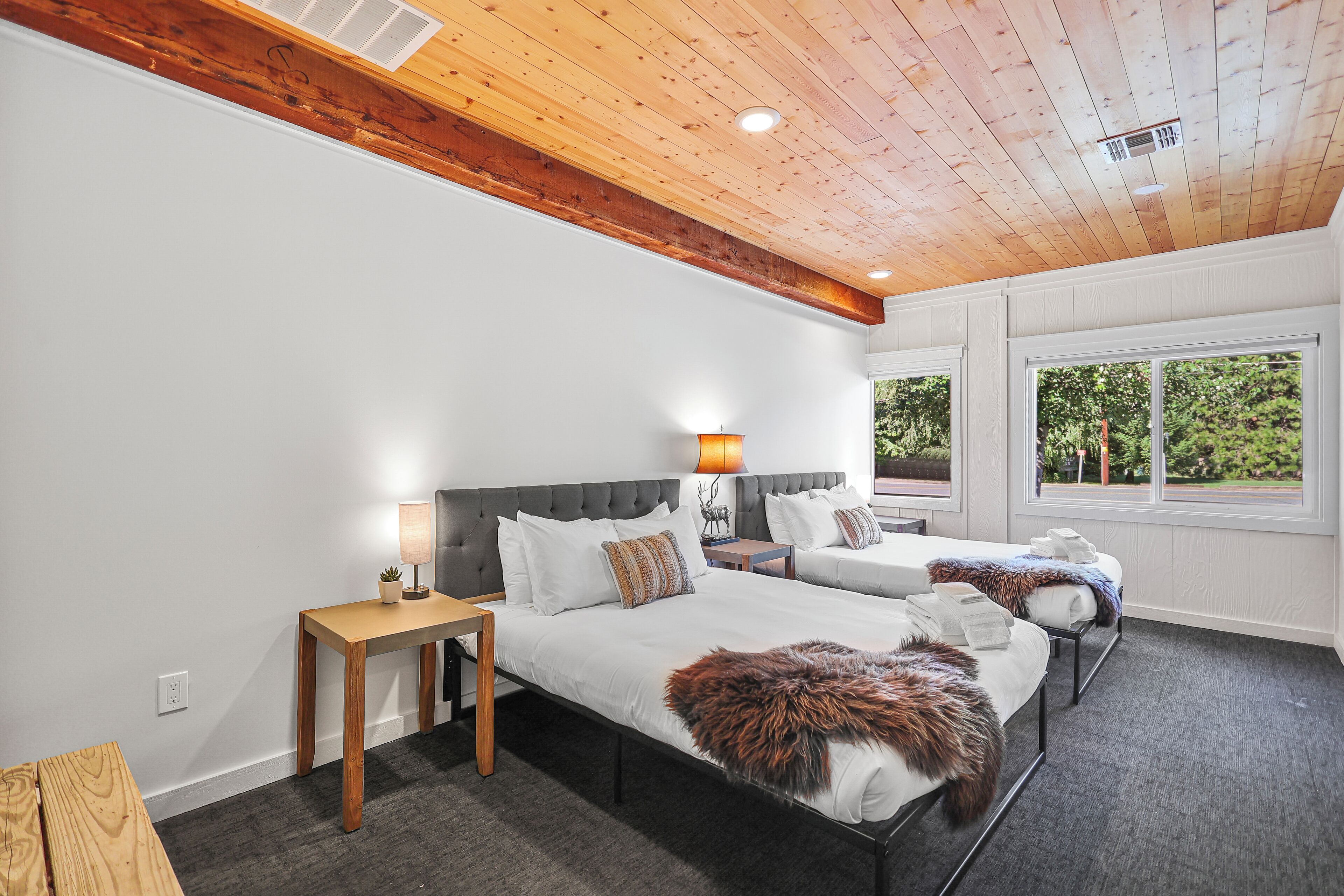 A hotel room with two beds, a wooden ceiling, and a window with a view of greenery.