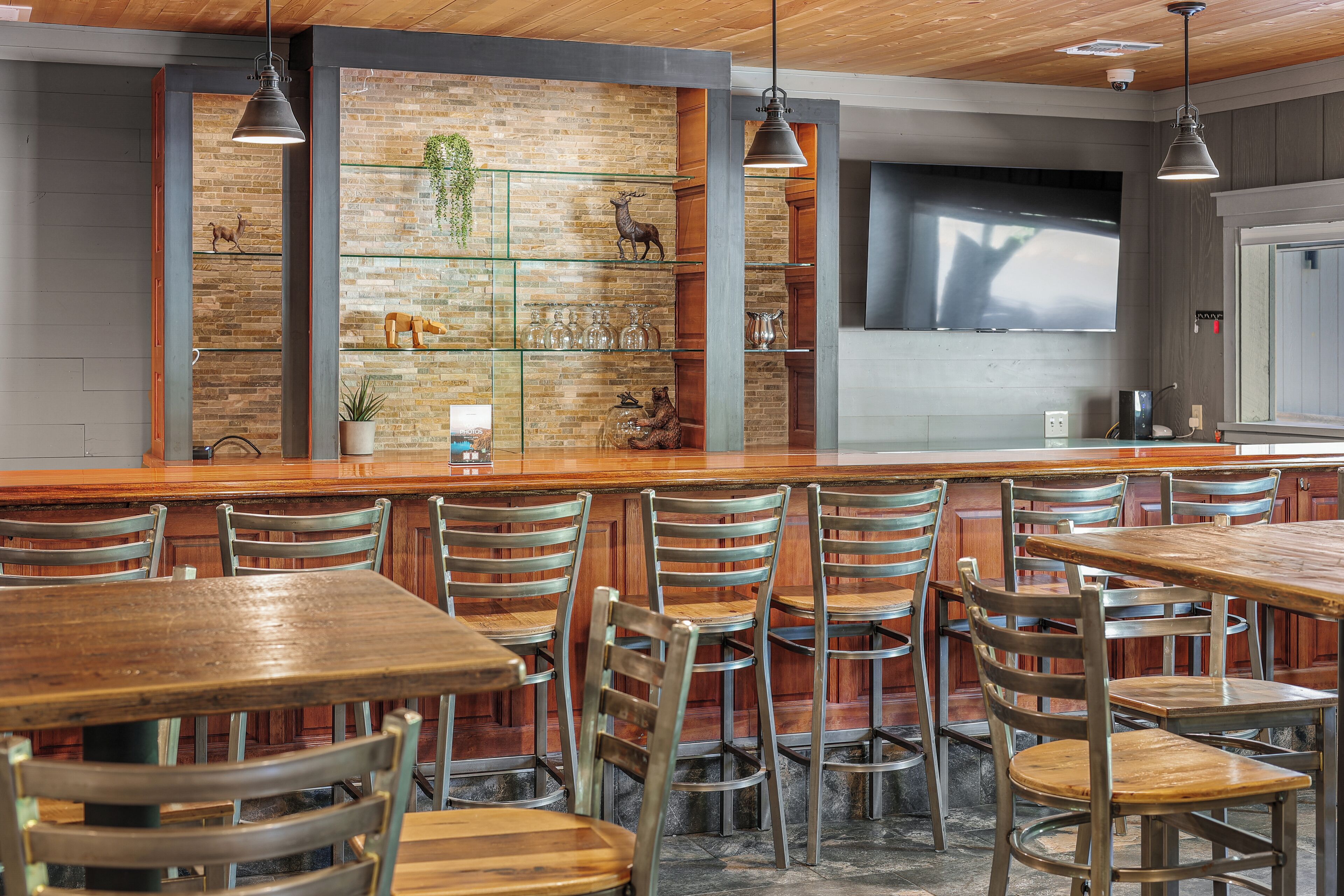 A restaurant with wooden tables and chairs, a brick wall with shelves displaying decorative items, and pendant lighting.