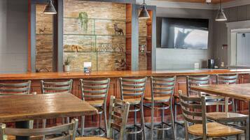 A restaurant with wooden tables and chairs, a brick wall with shelves displaying decorative items, and pendant lighting.