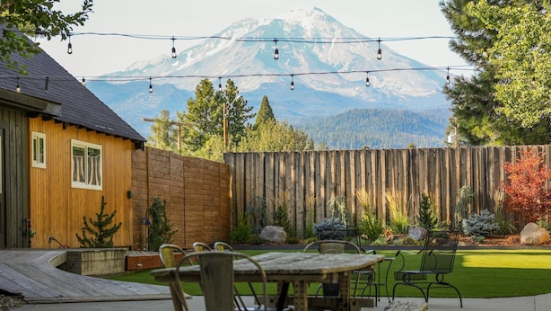 Une terrasse avec une table et des chaises en bois, une clôture en bois et une vue sur les montagnes.