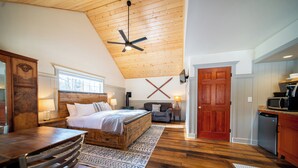 Une chambre avec un ventilateur de plafond en bois, un grand lit, un bureau en bois et une chaise.