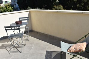 Un balcon avec une table et des chaises en métal, un panier en osier et un coussin à motifs.