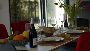 Une table dressée pour un dîner à deux, avec une bouteille de vin, un saladier de fruits et un vase de tulipes.
