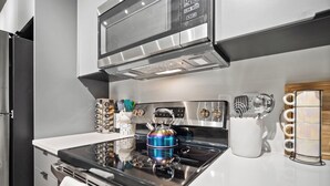 A modern kitchen with a stainless steel stove, microwave, and oven. There are utensils and a kettle on the counter.