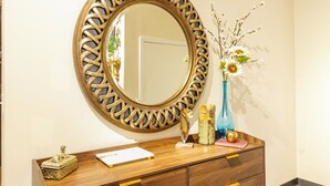 A wooden vanity with a decorative mirror, a vase with flowers, and a small statue.