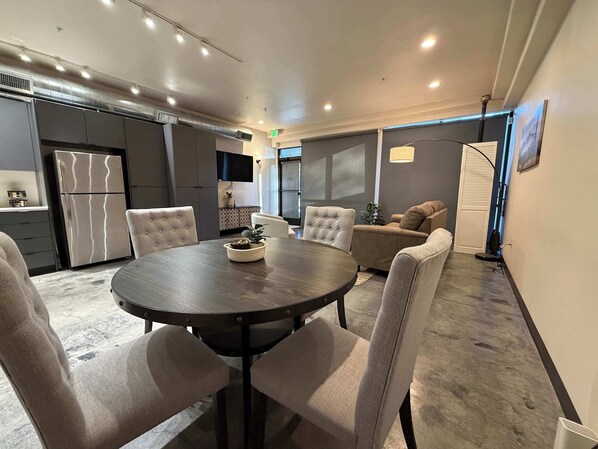 A modern dining area with a round table, cushioned chairs, and a built-in refrigerator.