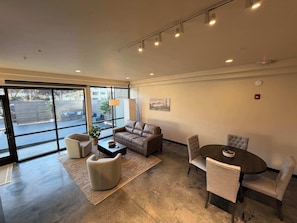 A modern interior with a leather sofa, a round table, and chairs. Large windows offer a view of the outside.